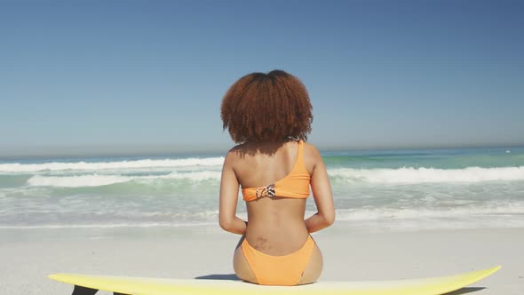 Rear view of African American woman sitting on her surfboard alt
