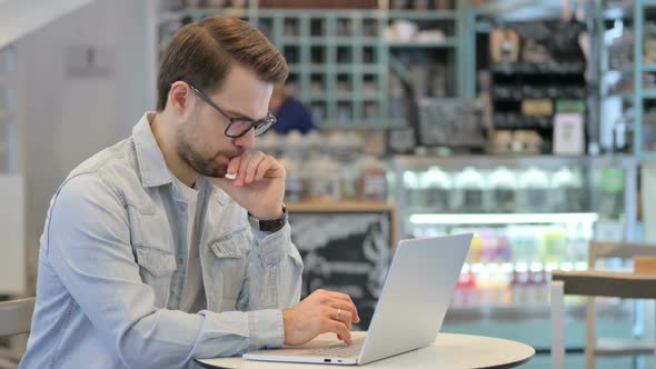 Man Thinking While Using Laptop in Cafe alt