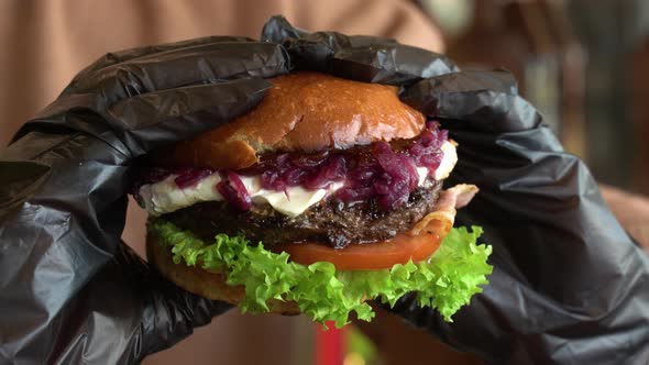 Hands in Black Gloves Crush a Burger