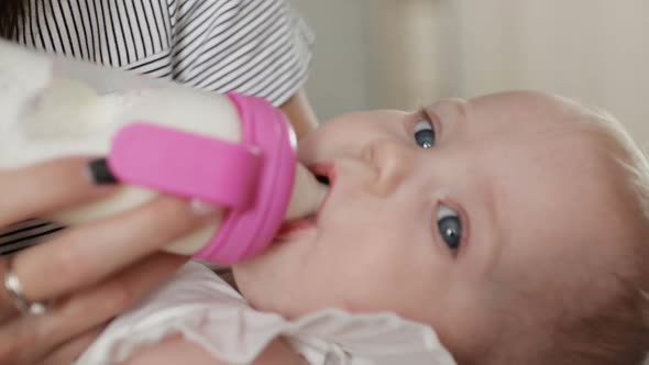 Small Baby Drinks Milk From Small Bottle in Hands of Mother