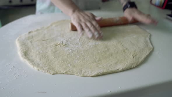 Housewife rolls out fresh dough with wooden rolling pin