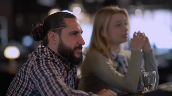 Anxious Worried Man Watching Sport Match Sitting at Bar Counter with Blurred Woman at Background alt