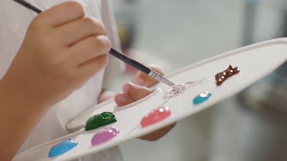Little Girls Hand Mixes Paints with Brush on Palette