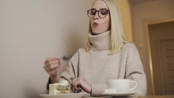Young Beautiful Woman in a Cozy Sweater Eats Sweet Cake and Drinks Aromatic Coffee
