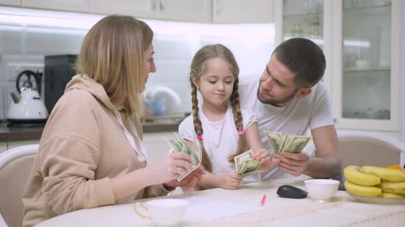 Joyful Caucasian Young Family Scattering Money in Slow Motion Resting in Kitchen at Home alt