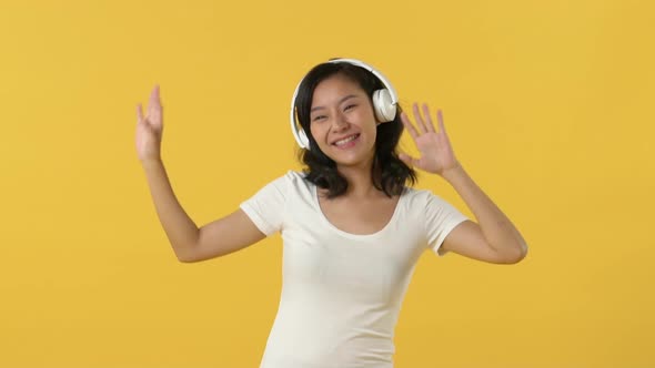 Happy beautiful young Asian woman dancing with hands moving up while listening to music