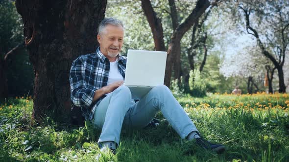 An Elderly Whitehaired Man with a Laptop is Excited and Rejoices in an Online Victory or Good News