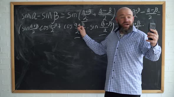 Adult Male Teacher Looking at the Camera of His Smartphone During a Math or Algebra Lesson alt