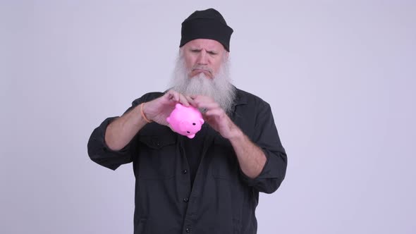 Mature Bearded Hipster Man Shaking Piggy Bank and Looking Sad alt