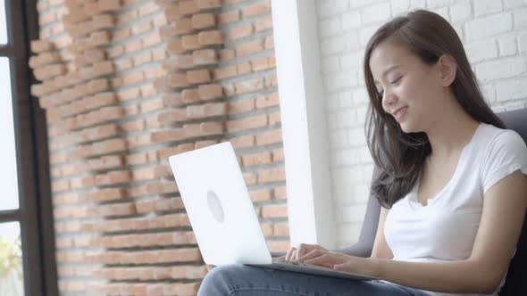 Young asian woman working laptop computer with smile and happy sitting on couch at living room. alt