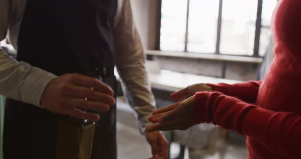 Midsection of man working at cafe bar, using sanitising spray on hands of female colleague alt