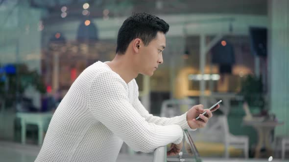 Profile of Asian Male Scrolling Phone on Background of Big Windows