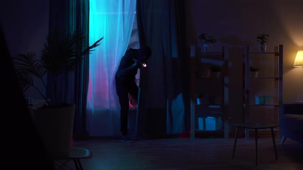 Thief in a Balaclava Climbs Through the Window of an Apartment alt