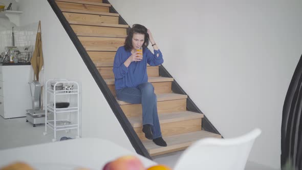 Wide Shot of Elegant Caucasian Brunette Woman Drinking Orange Juice in the Morning at Home. Portrait alt