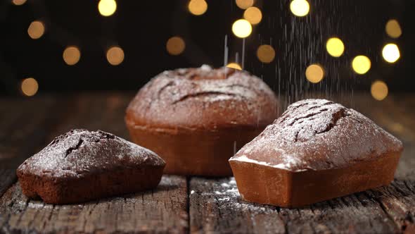 Three Christmas Breads Stollen Are Stacked on a Wooden Textured Table Sprinkled with Powdered Sugar alt