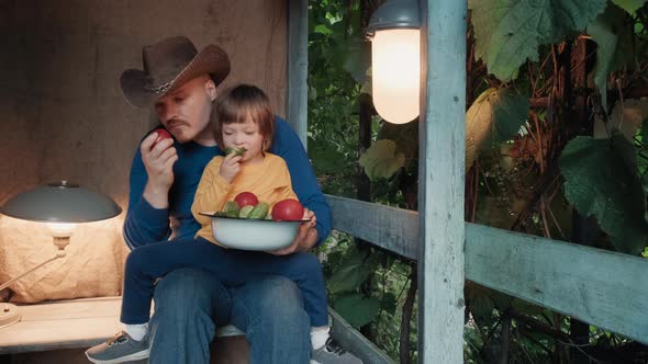 Father and Small Child Eat Fresh Organic Vegetables From Farm Sitting on Porch alt