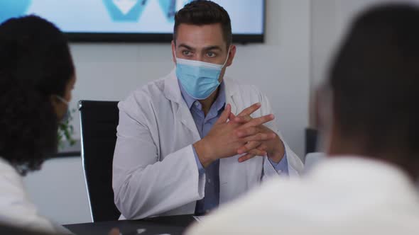 Mixed race male doctor wearing mask giving presentation in meeting room gesturing alt
