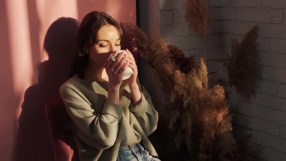 Beautiful Woman Sitting Near Window and Enjoy a Cupt of Tea on Background of Sunset alt