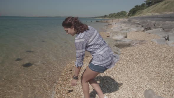 Close Up Shot Of Young Woman Reaching Down To Pick Up Plastic Bottle On Beach In Slowmotion alt