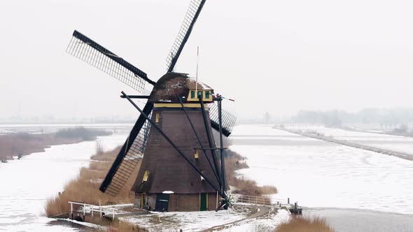 Line of old world heritage Kinderdijk windmills with front spinning by icy canal alt