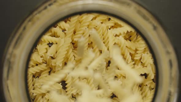 TOP VIEW: Uncooked Spiral Pasta Fall Into Glass Jar On Black Background - Slow Motion alt
