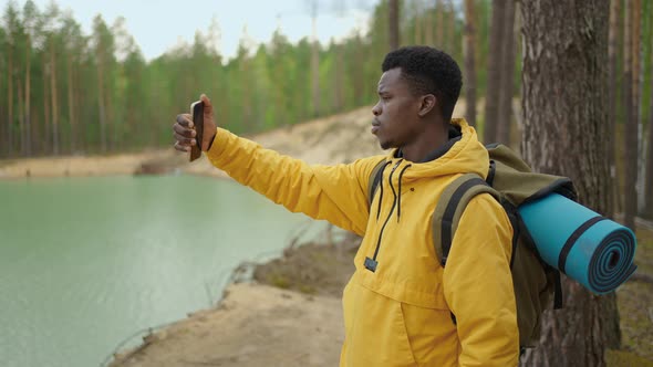 A Black Man is Walking on Top of a Mountain and Typing a Message and Photo on His Smartphone alt