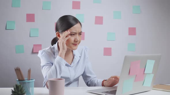 Asian woman working on a laptop has headache sitting