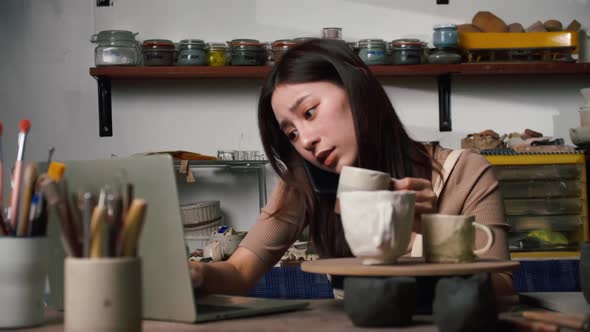 A young female ceramicist is busy checking orders for ceramics for a customer. alt