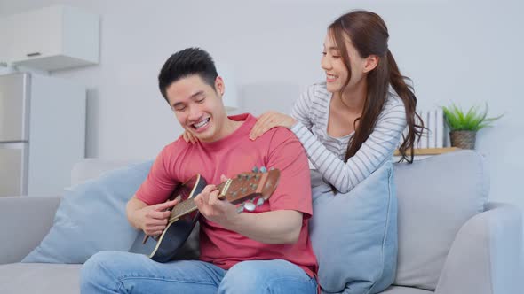Asian young loving couple play guitar together in living room at home. alt