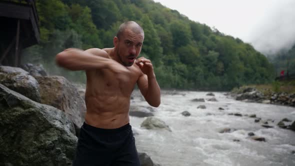 an Unshaven Man with a Bare Torso Trains By the River Against the Background of Mountains alt