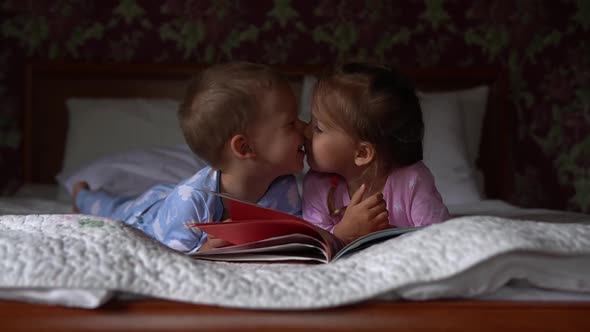 Two Cute Smiling Preshool Toddler Children on Pajamas Read Book of Fairy Tales on Bed alt