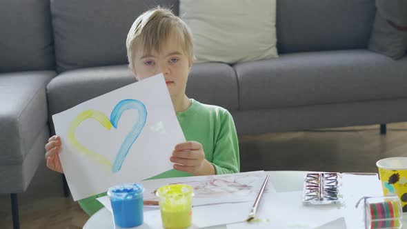 Boy with Down Syndrome Holding a Picture with Yellow and Blue Heart