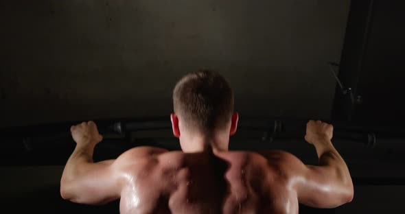 A man with beautiful muscles on his back, in the gym, pulls himself up on a horizontal bar alt