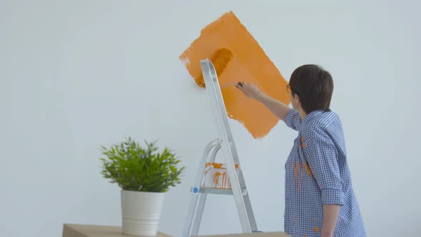 Flat Renovation Concept. Happy Middle-aged Woman Painting White Wall with Paint Roller, Orange Paint alt