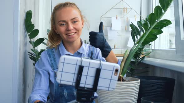 Gardener Woman Blogger Using Phone While Transplants Indoor Plants and Use a Shovel on Table alt