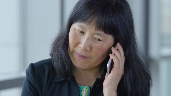 Mature Asian businesswoman using cell phone in office lobby