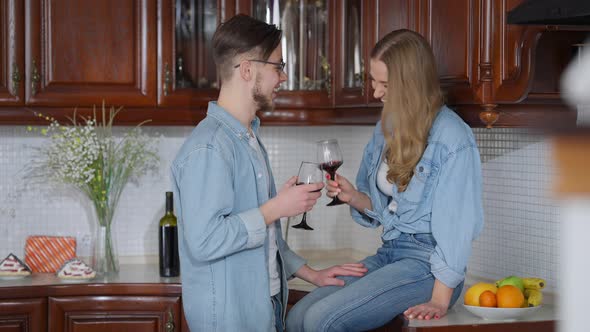 Carefree Beautiful Young Woman Sitting on Kitchen Countertop As Handsome Man Toasting alt