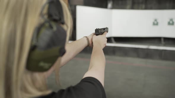 Rear View of a Blond Woman Aiming at a Target in a Shooting Gallery Holding a Gun in Her Hands