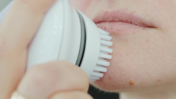 Young woman cleaning face using cosmetic face brush. Facial. Cosmetic procedures.