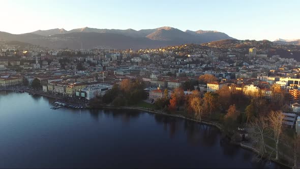 A drone view of a beautiful town surrounded by mountains, next to a lake, during a sunset in autumn. alt