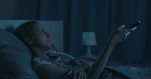 Woman lying in bed and watching TV late at night, she is sleepy and yawning