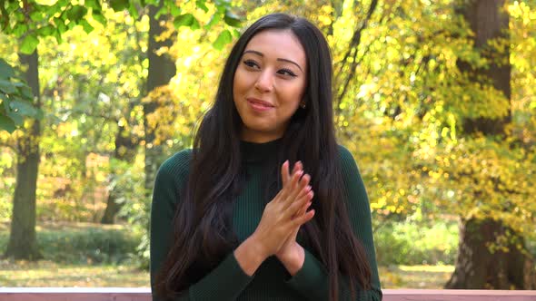 A Young Asian Woman Sits on A Bench in A Park and Celebrates alt