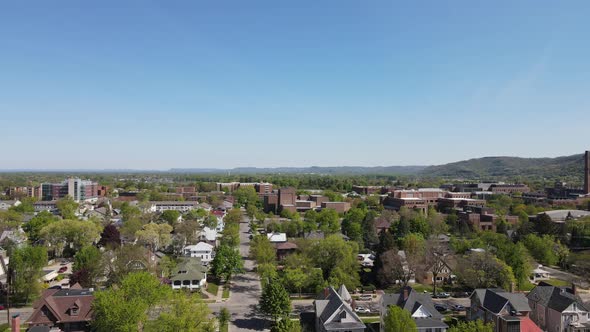 Aerial view of tree lined streets, single family homes, blue sky, mountains and forest on summer day