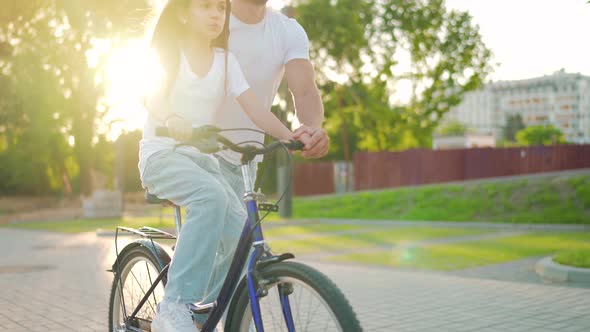 Dad is Teaching Daughter How to Ride Bicycle at Sunset alt