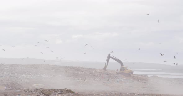 Digger clearing rubbish piled on a landfill full of trash alt