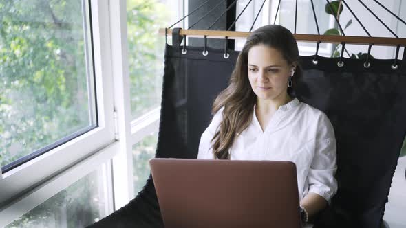 Woman Uses Video Chat on Laptop Lying in Hammock in Flat