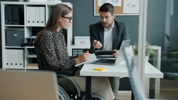 Office Workers Handicapped Woman in Wheelchair and Young Man Talking in Workplace alt