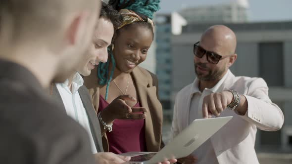 Happy Coworkers Standing on Rooftop and Looking at Laptop