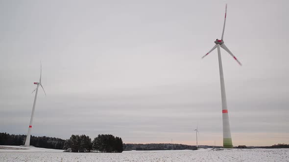 Low angle shot of rotating wind turbines on a snowy field in Germany. Wide shot of a wind farm.