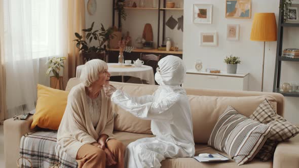 Doctor in Protective Suit Checking Throat of Elderly Woman alt